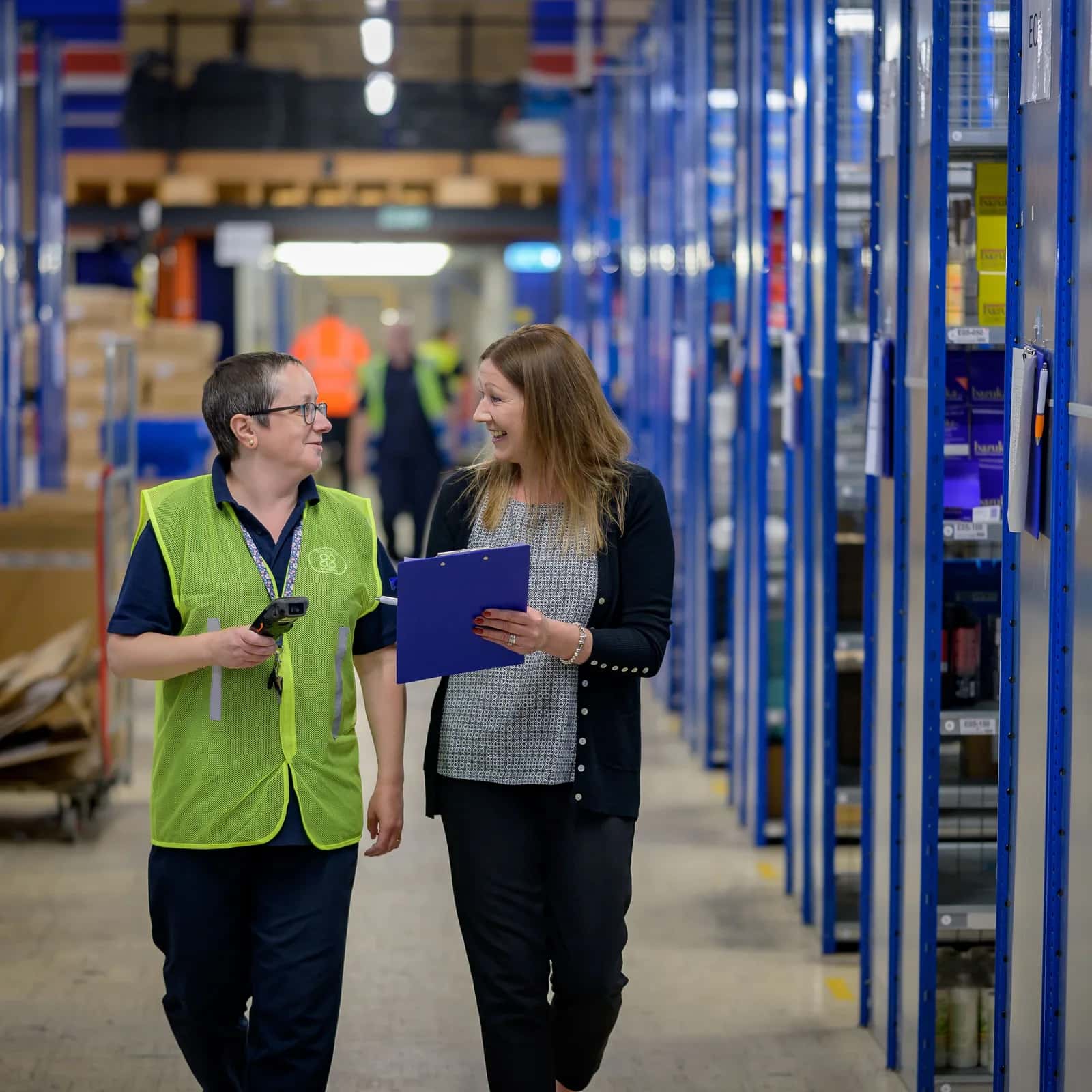 Two warehouse staff walking between loaded storage racks