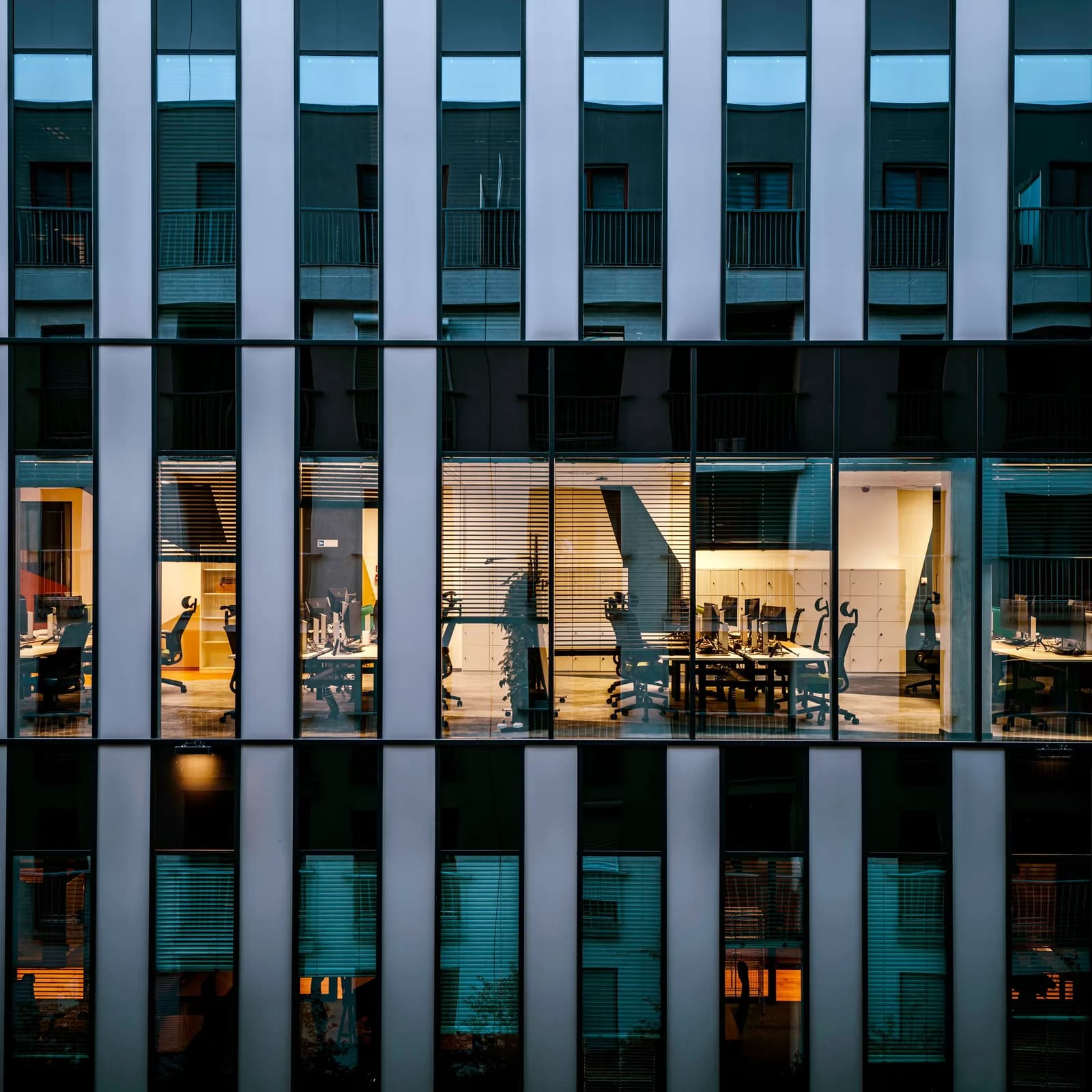 Lit offices behind the facade of a modern building at dusk